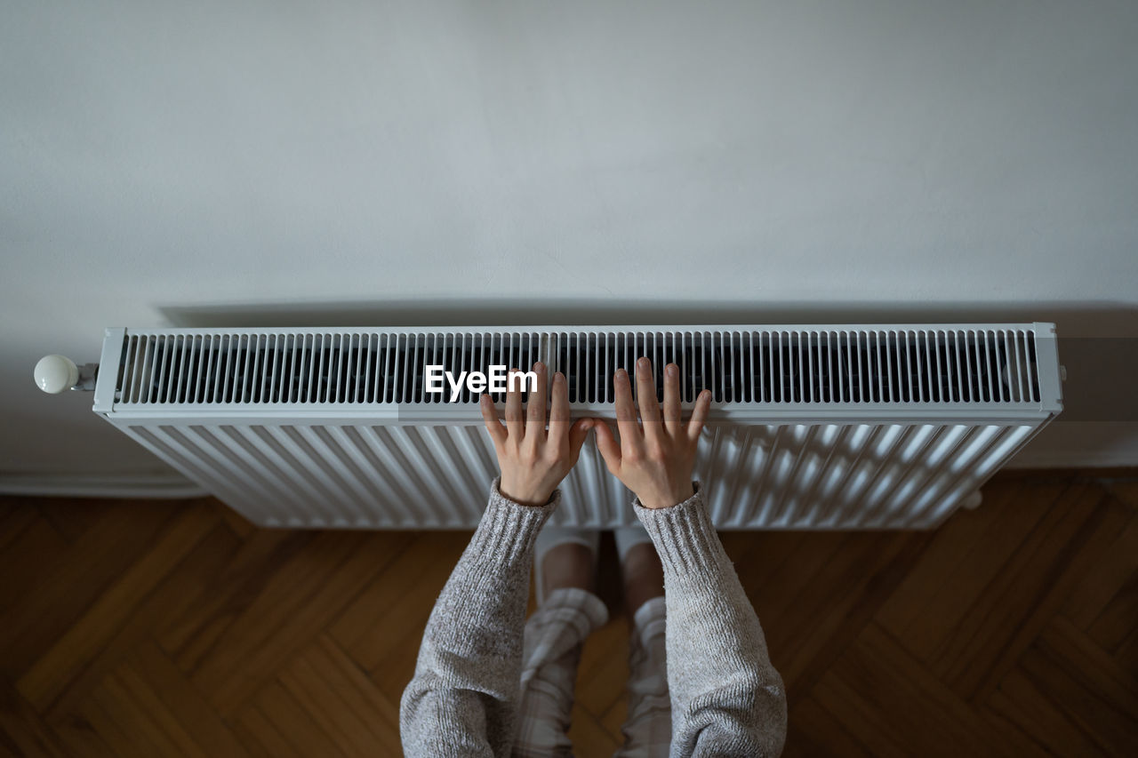 Woman in woolen sweatshirt tries to catch stream of warm air from central heater touching device