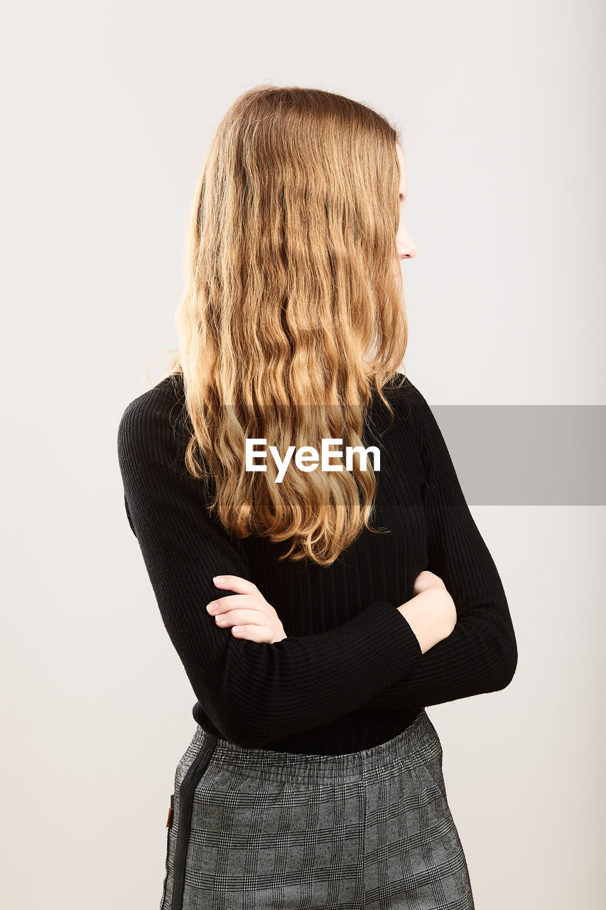 Teenage girl with blond hair standing against white background