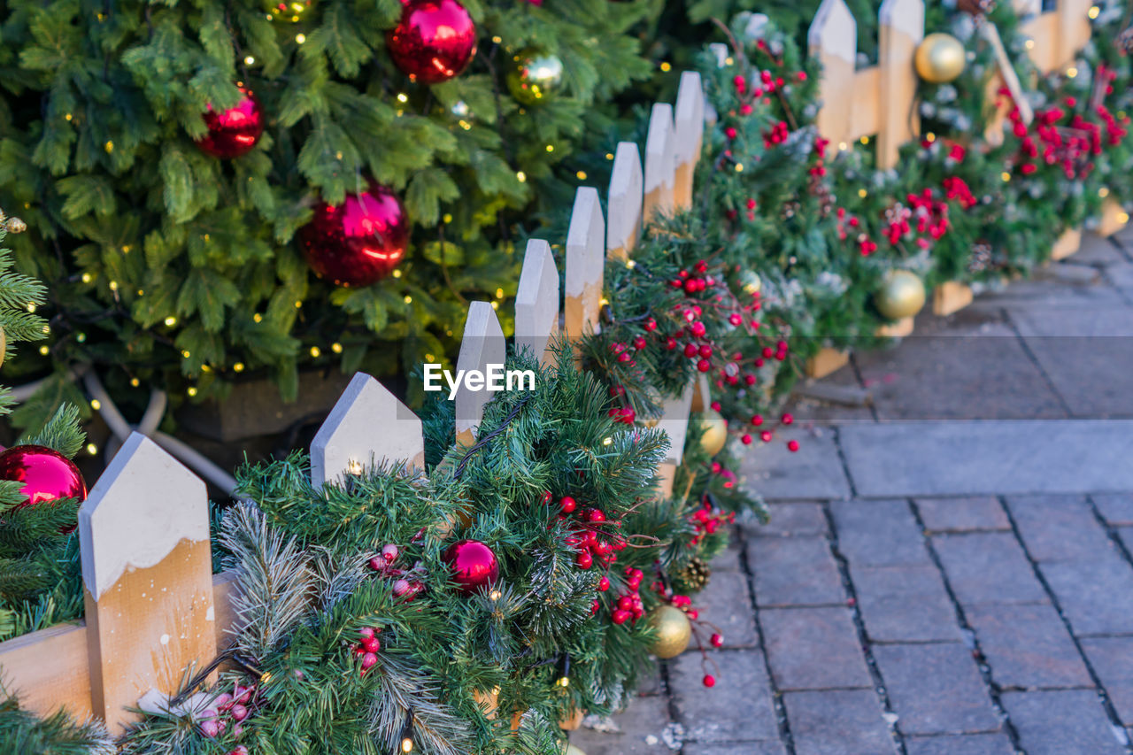 Christmas outdoors decoration of fence. branches with balls and garland