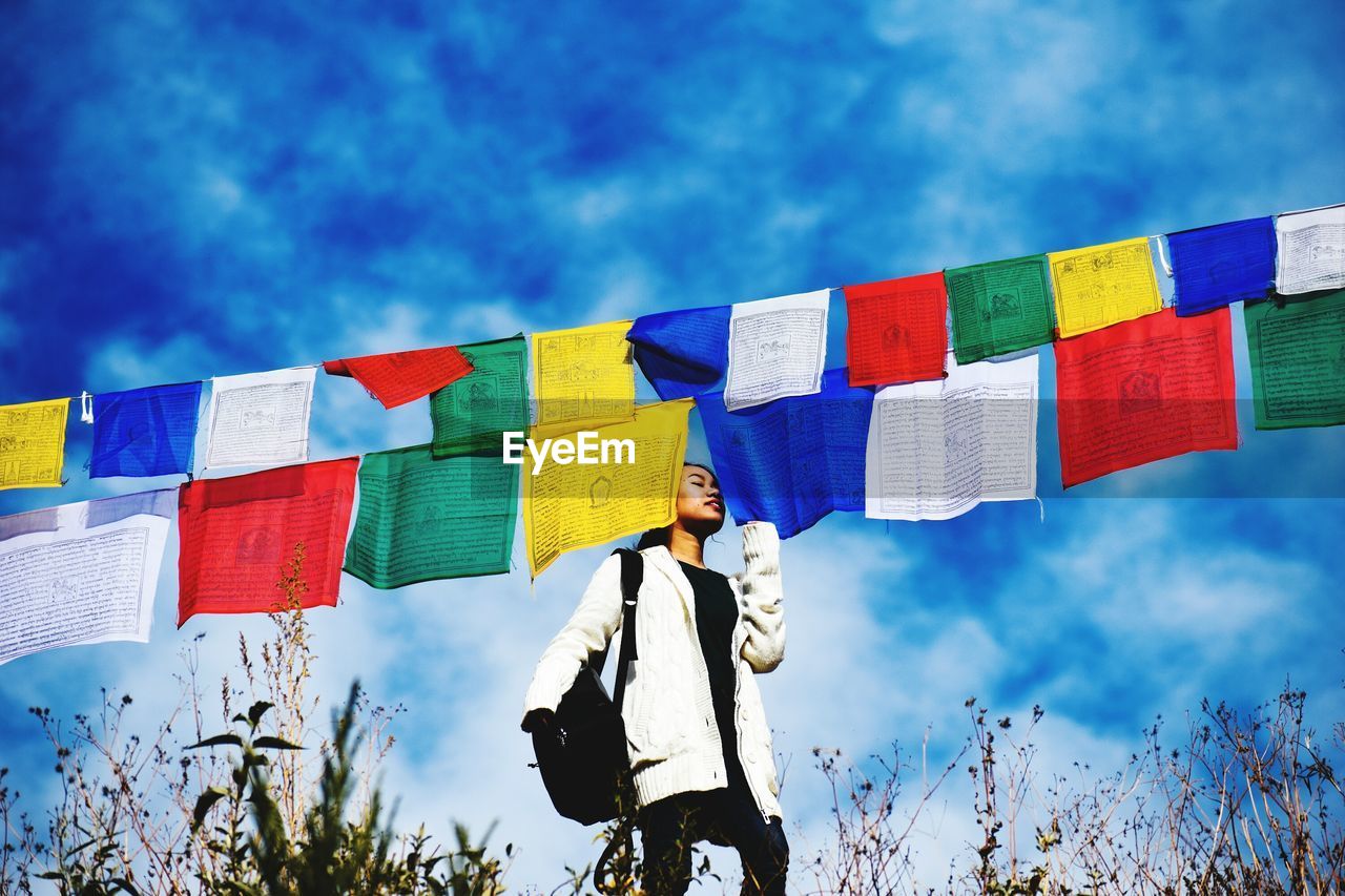 Low angle view of young woman standing by flags against sky