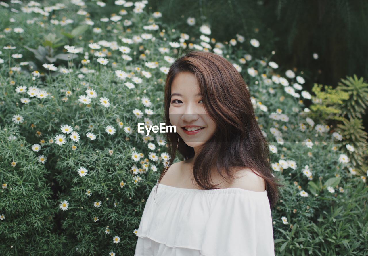 Portrait of smiling young woman by plants at public park