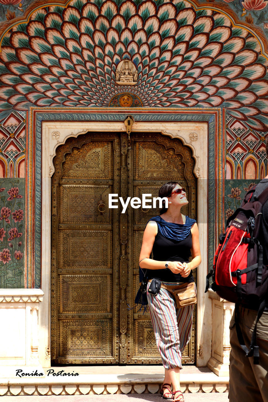 PORTRAIT OF YOUNG WOMAN STANDING BY DOOR