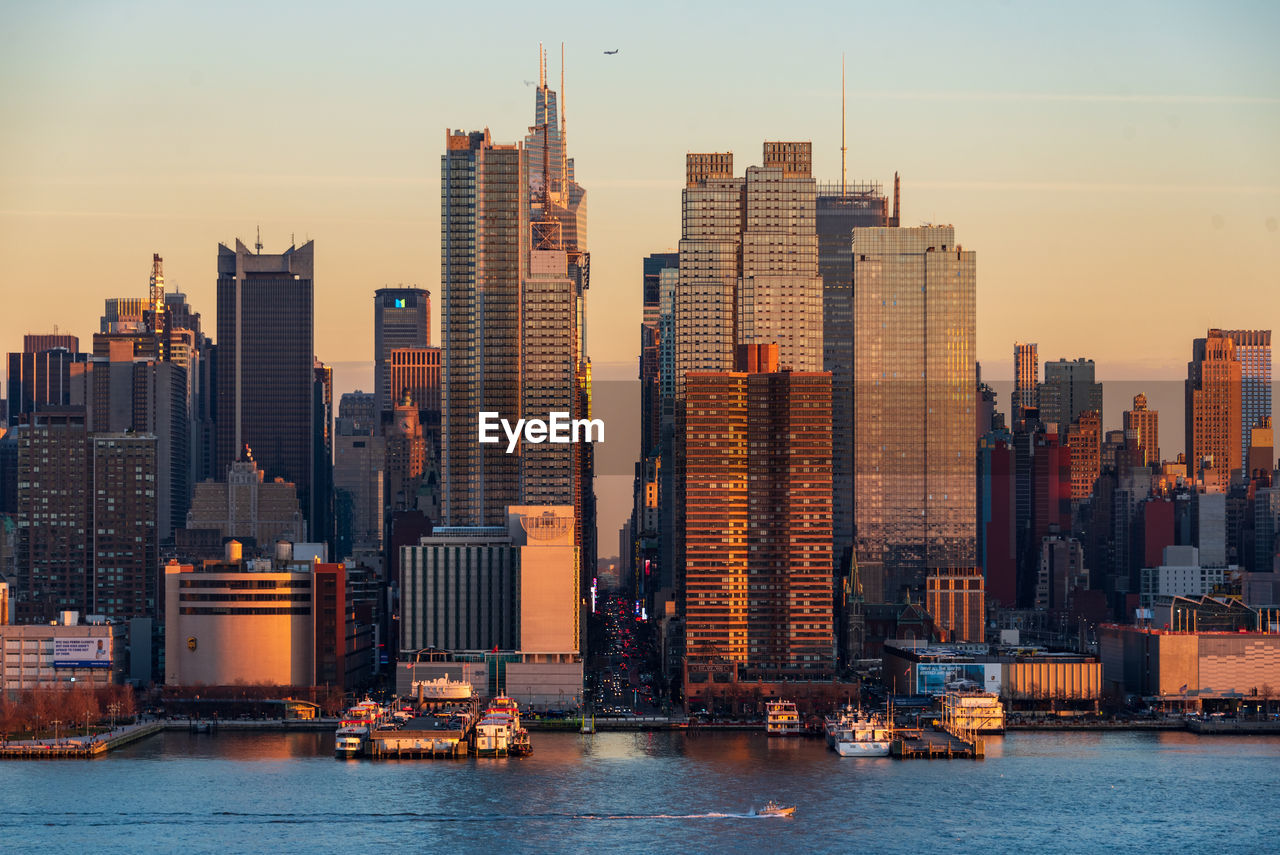 Sea by buildings against sky during sunset