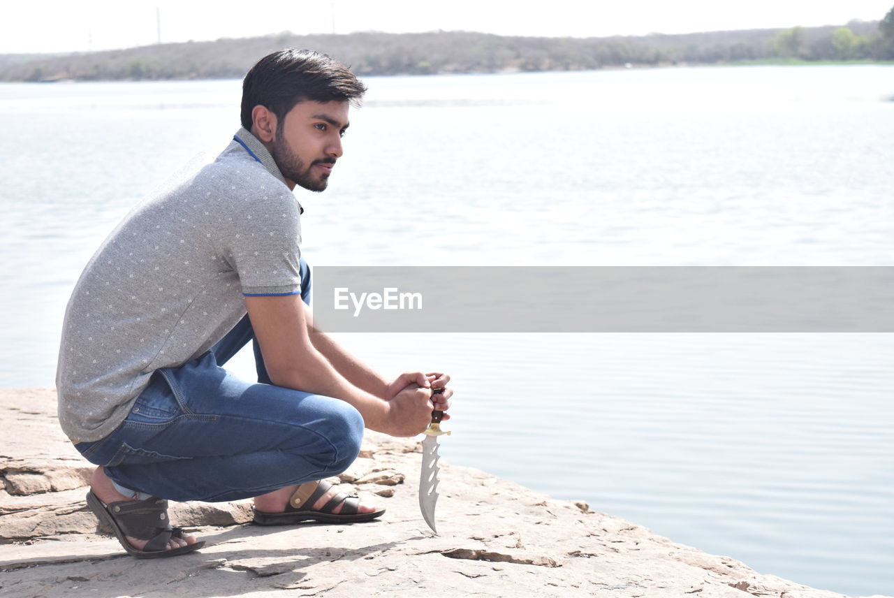 Side view of young man in squatting position at beach