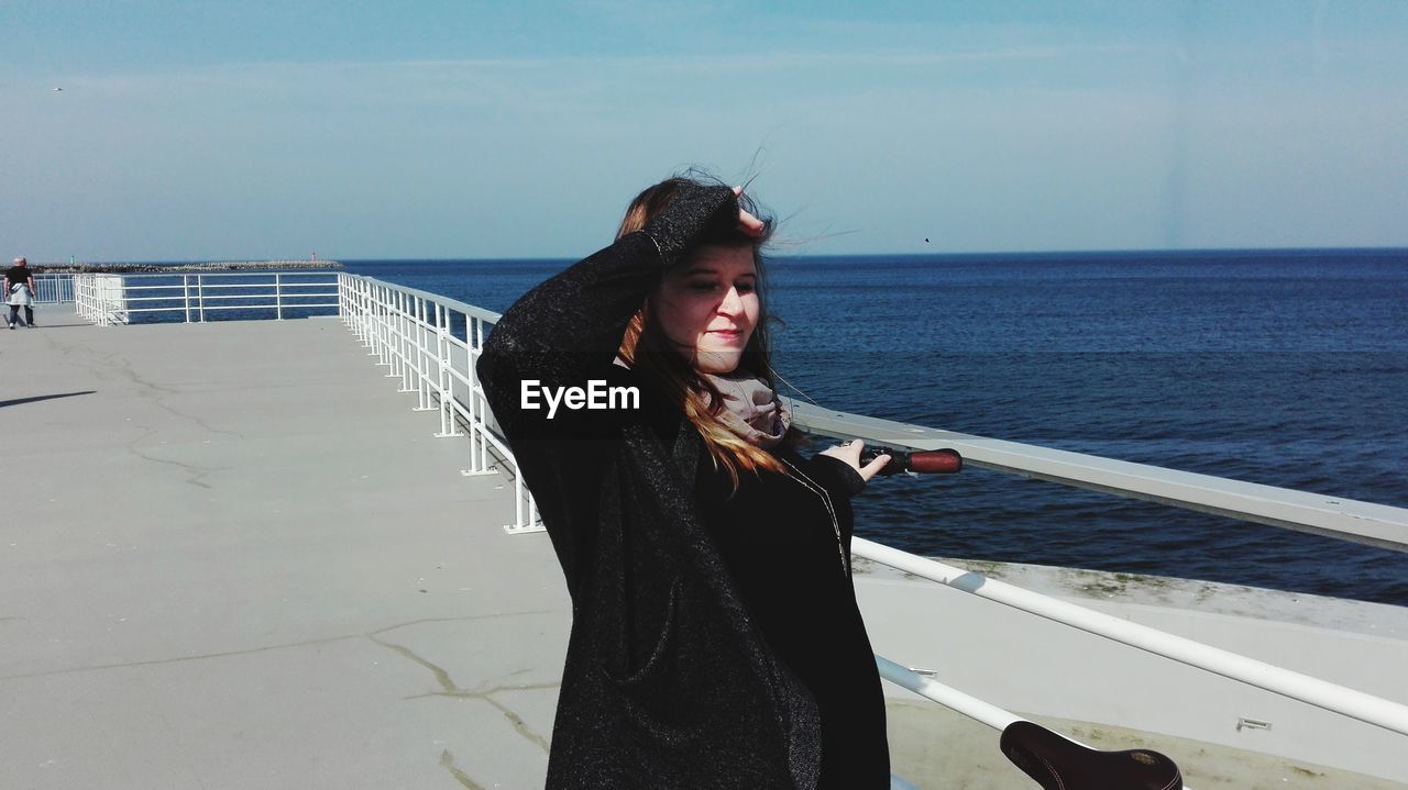 Woman shielding eyes on pier over sea against sky