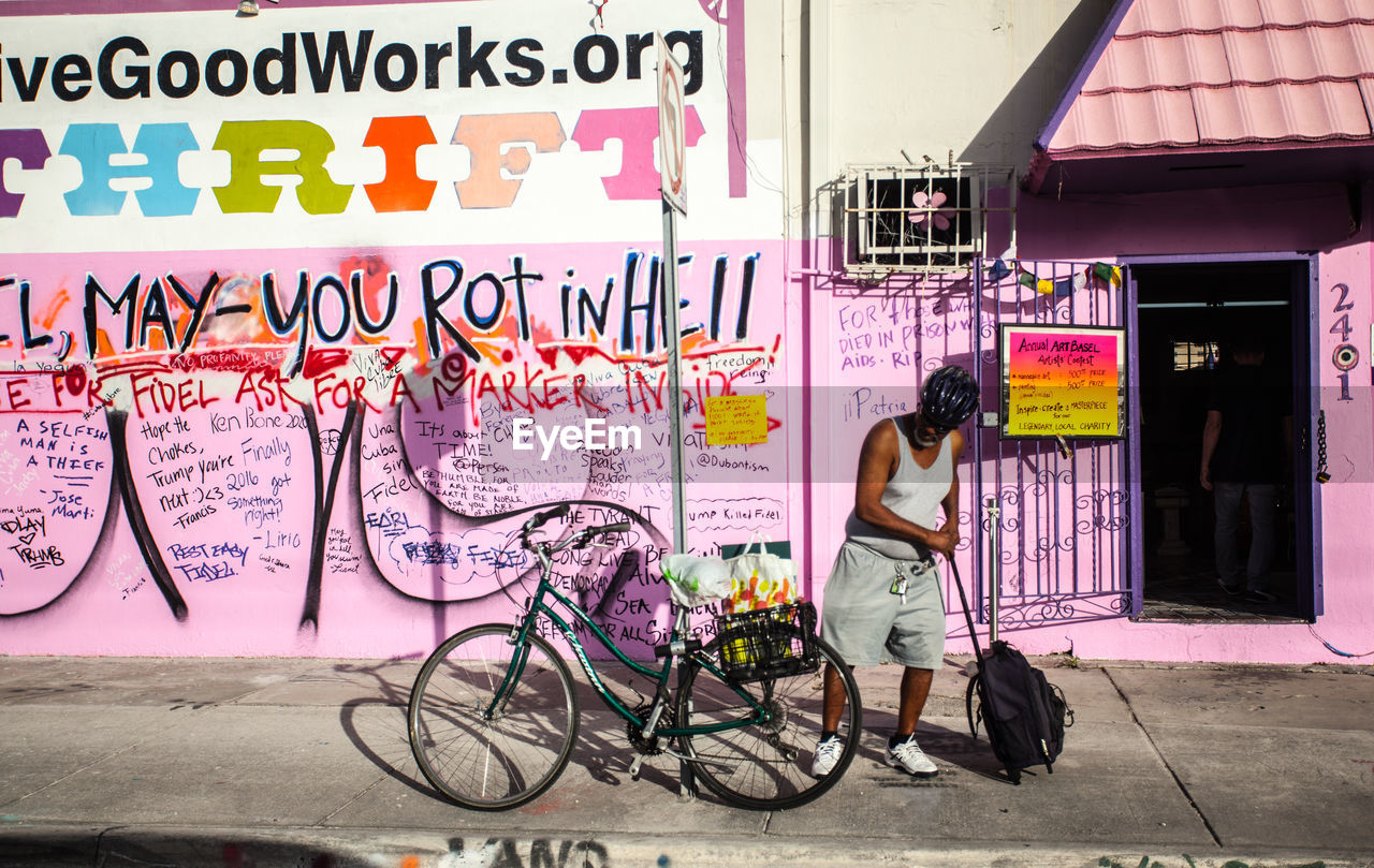 FULL LENGTH OF MAN WITH BICYCLE IN BACKGROUND