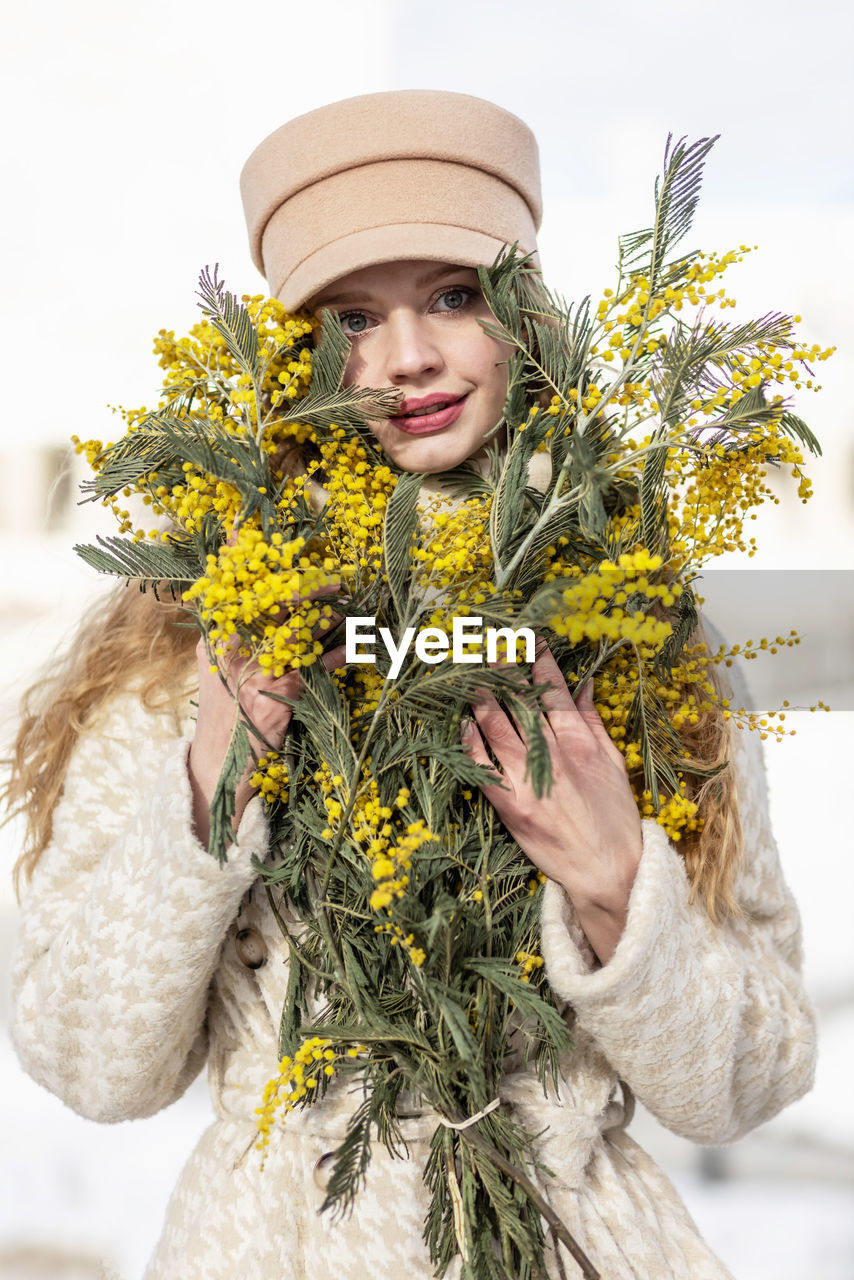 yellow, one person, plant, spring, adult, nature, portrait, clothing, flower, hat, smiling, happiness, floristry, women, holding, emotion, looking at camera, floral design, front view, flowering plant, young adult, bouquet, waist up, winter, outdoors, standing, female, cheerful, day, celebration, person, freshness, lifestyles, fashion accessory