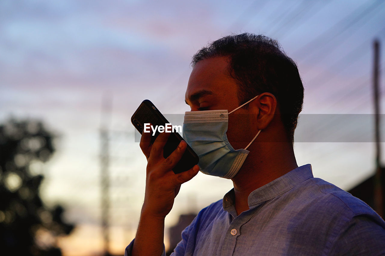 Man wearing ask talking on phone during sunset