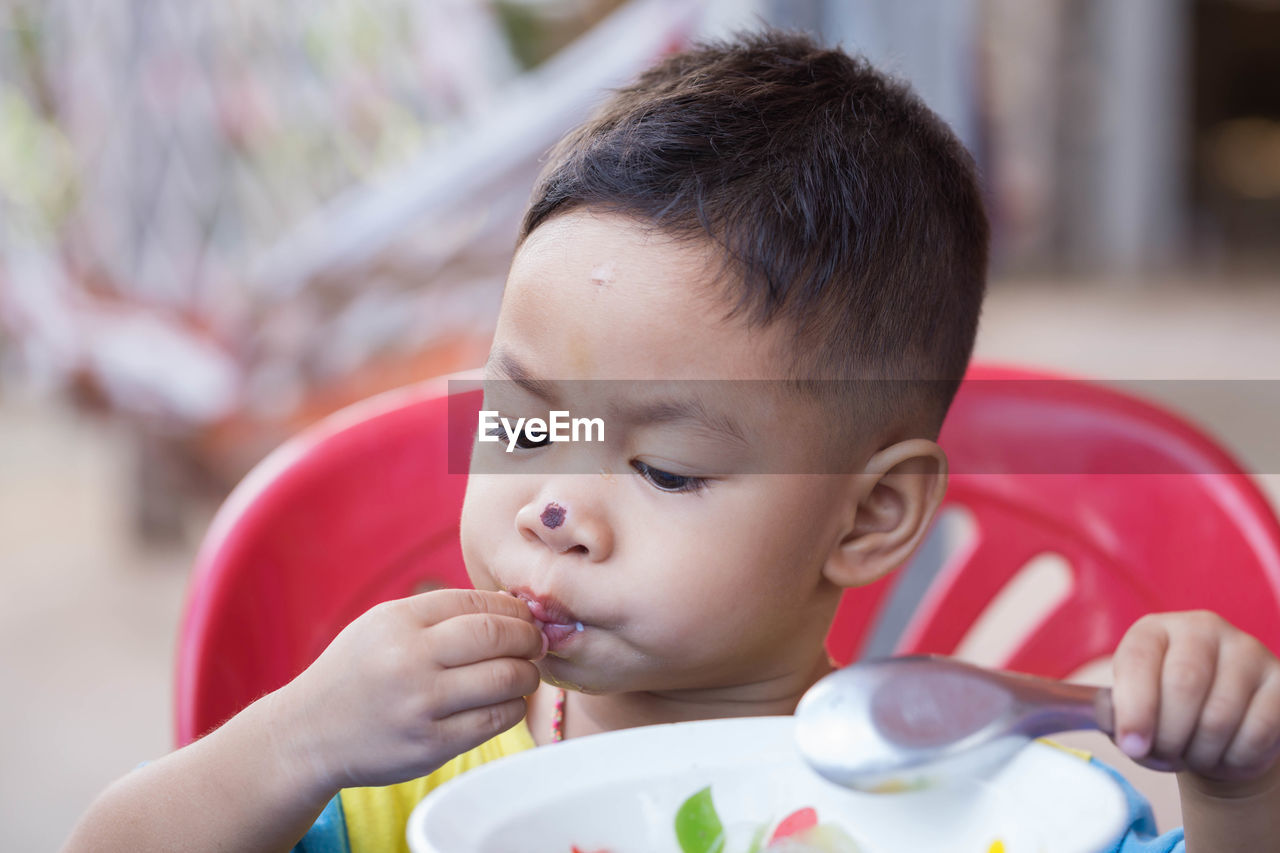 Close-up of cute boy with nose injury eating food while sitting at home