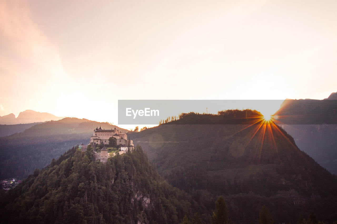 Medieval hohenwerfen castle towering over the austrian town of werfen at sunset turns pink-orange.