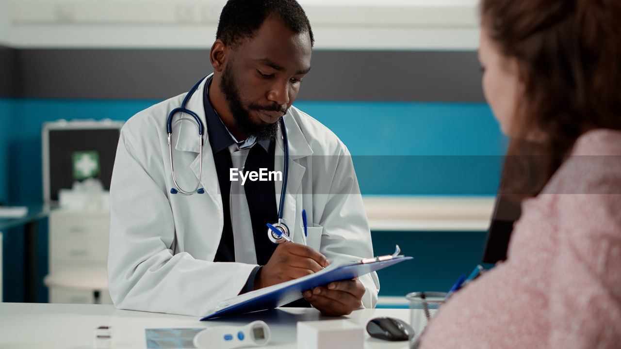 Doctor writing on paper sitting in front of patient at clinic