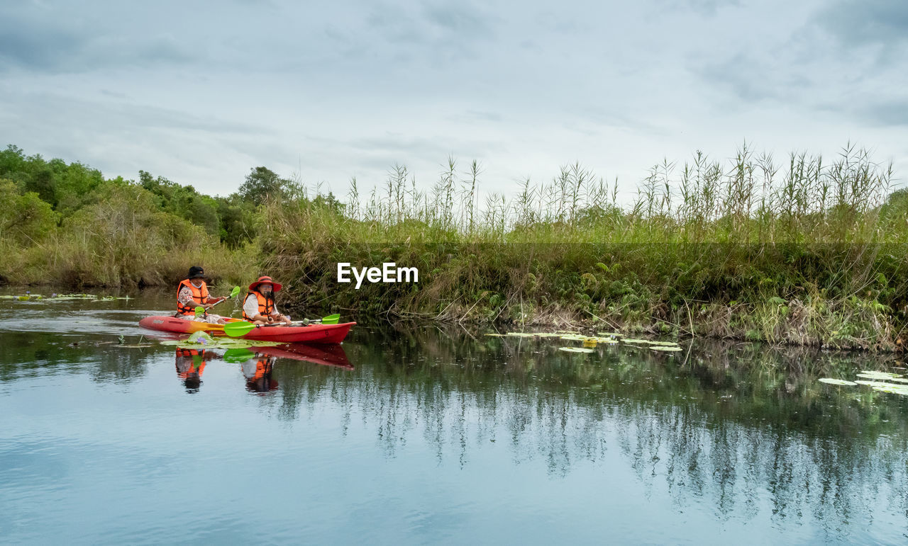 PEOPLE SITTING ON BOAT AGAINST LAKE