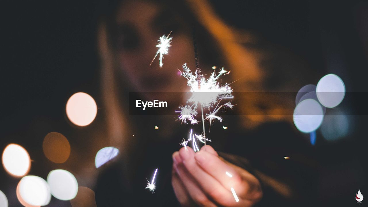 Low angle view of woman burning sparkler while standing on street at night