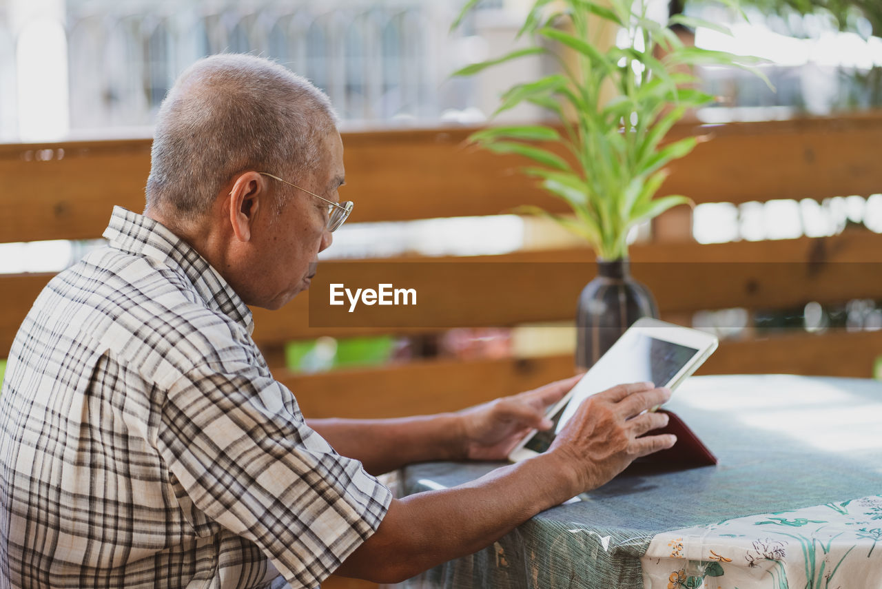 Side view of man using mobile phone while sitting on table