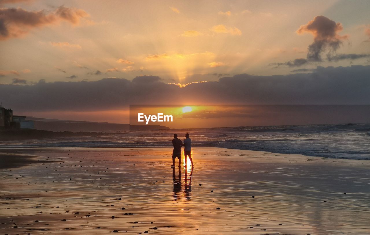 People standing on beach against sky during sunset