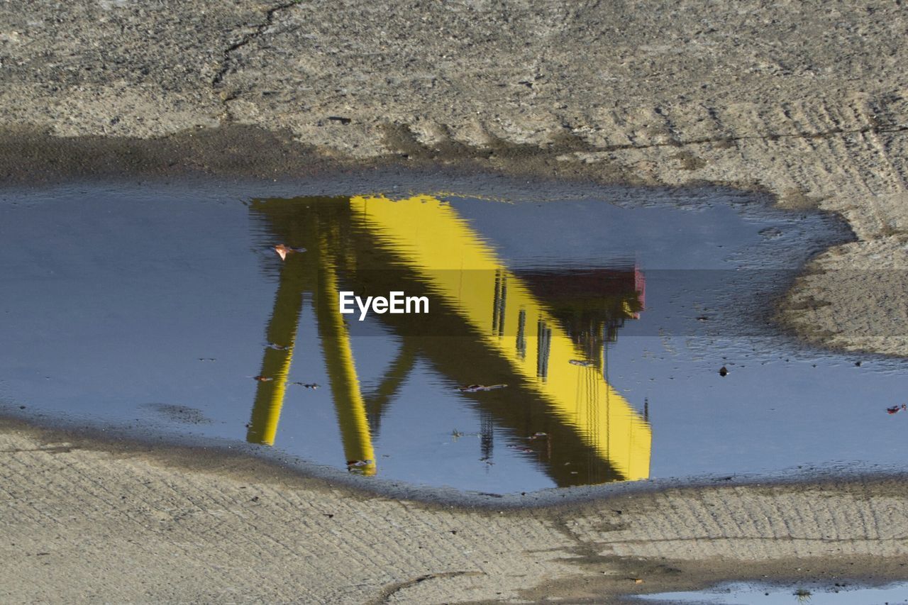 High angle view of yellow crane reflecting on puddle at construction site