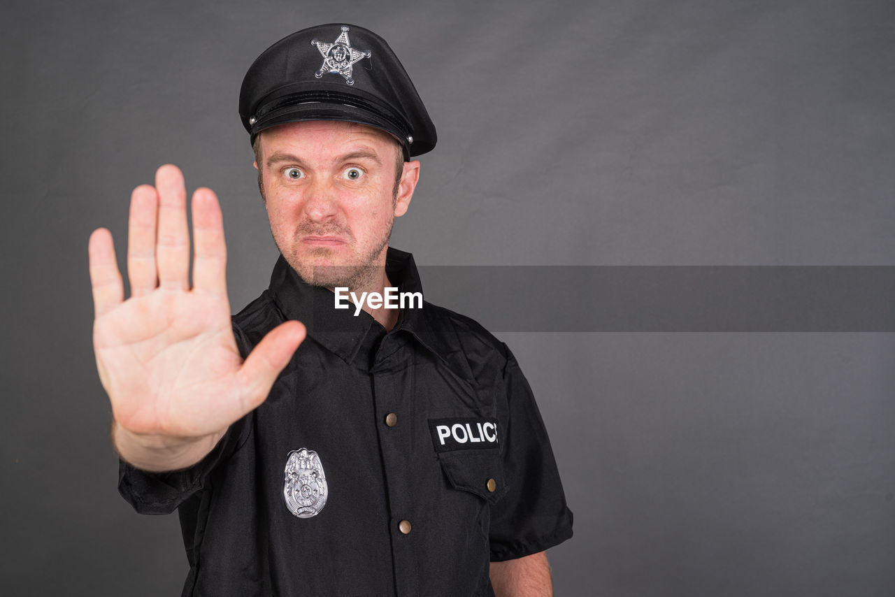 portrait, looking at camera, studio shot, one person, protection, security, uniform, police force, adult, government, person, law, clothing, gesturing, men, authority, hand, serious, black, occupation, standing, badge, indoors, front view, cut out, cap, mature adult, waist up
