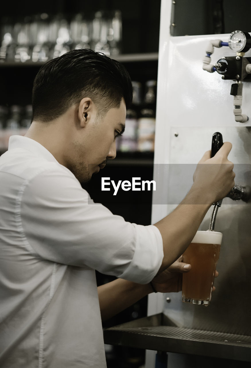 Side view of man pouring beer from tap in restaurant