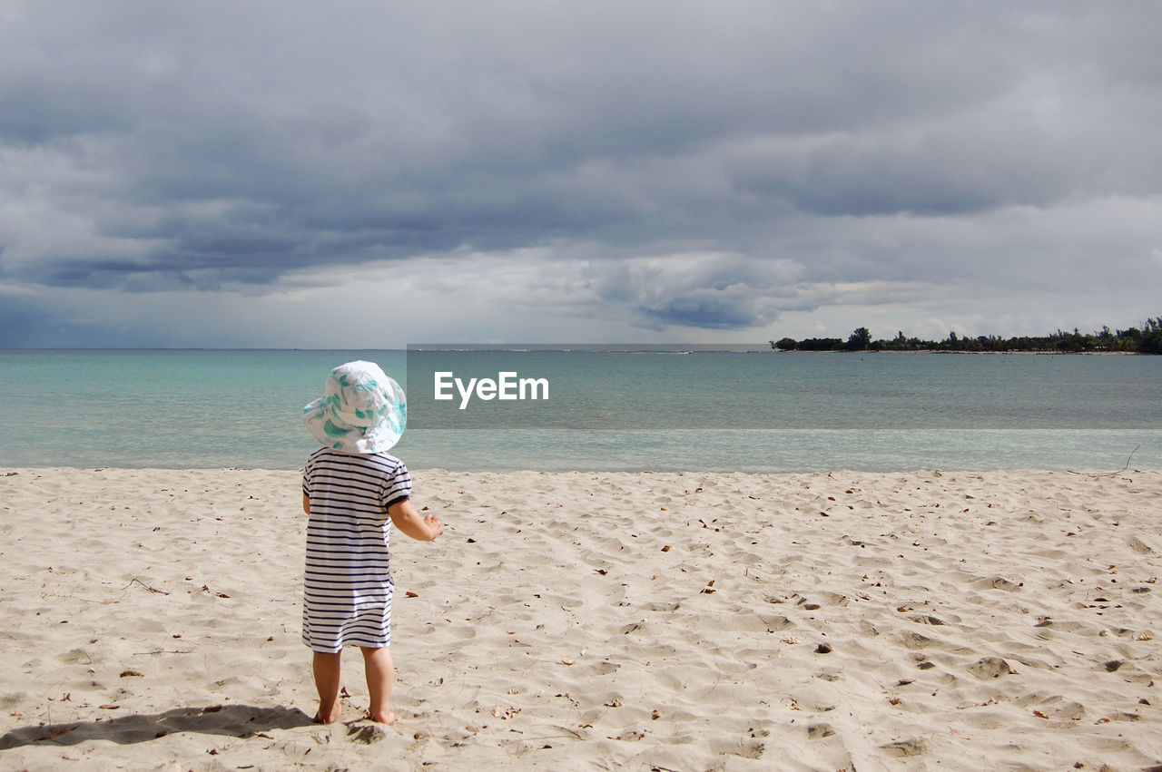 Rear view of toddler girl on beach against sky