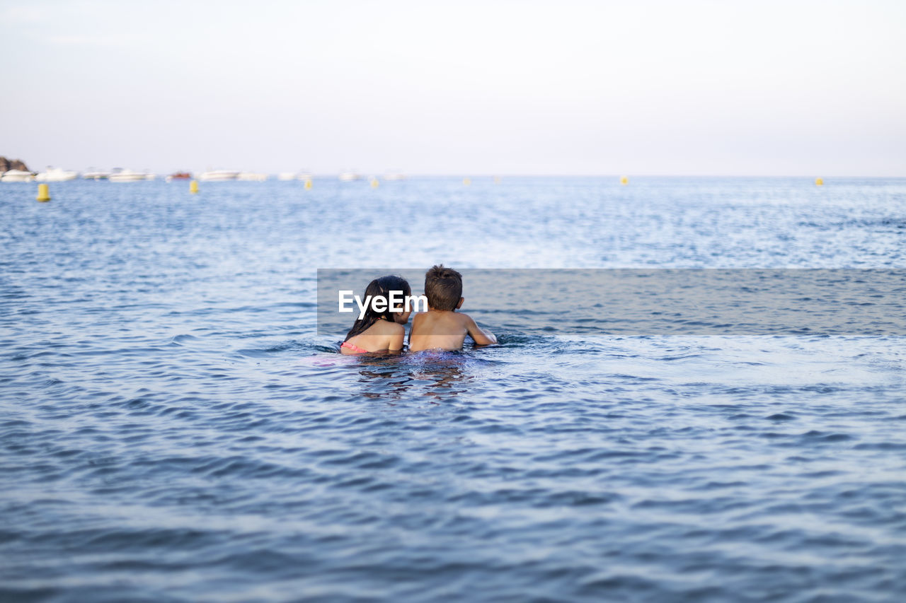 Rear view of siblings swimming in sea