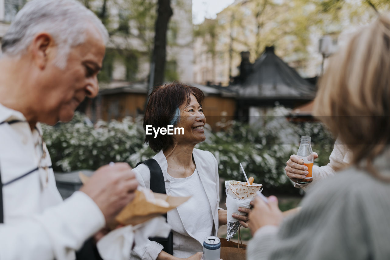 Smiling senior woman enjoying snacks with friends while standing at street