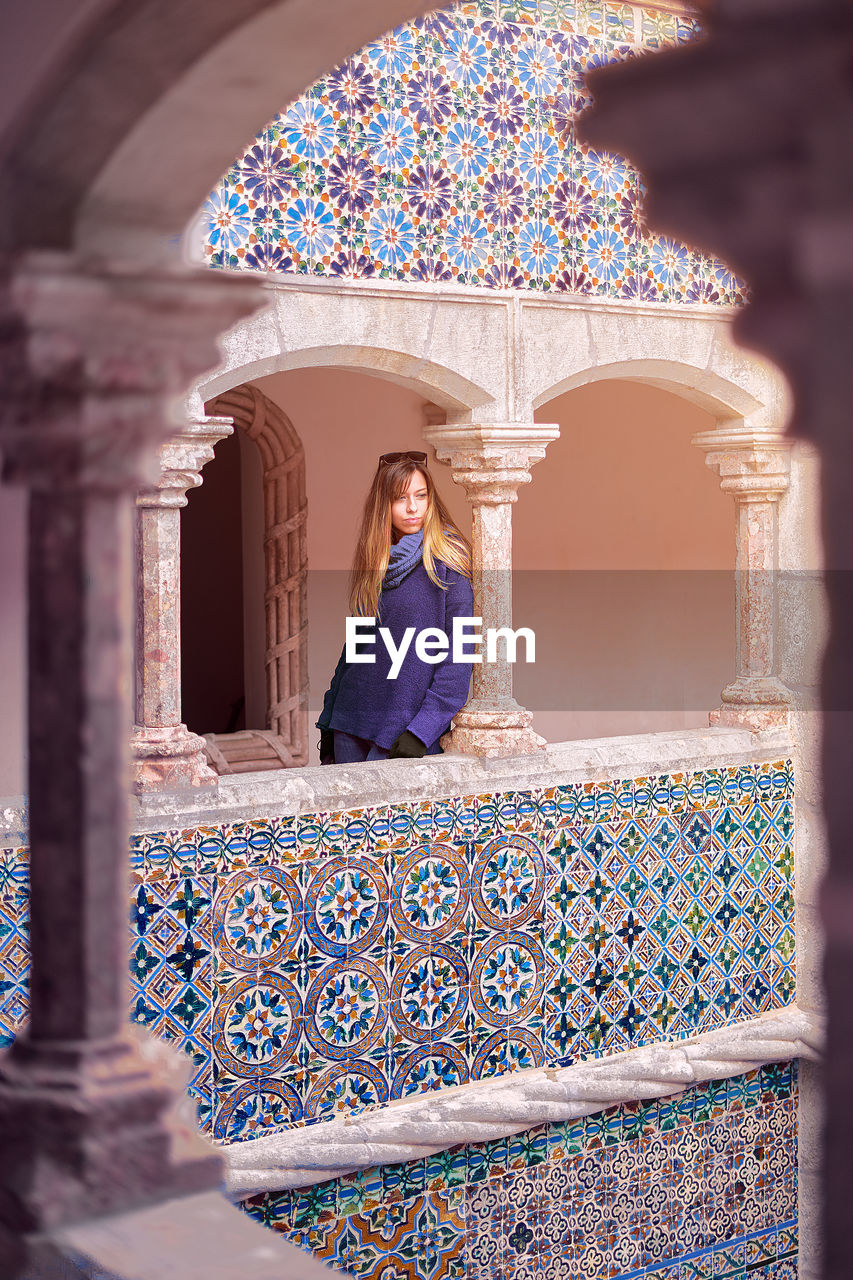 WOMAN STANDING AGAINST WALL OF COLUMNS