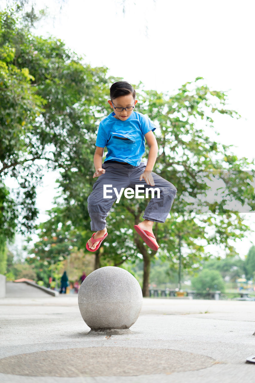 Outdoor portrait of a cute malaysian little boy trying to jump from a concrete ball at the park.