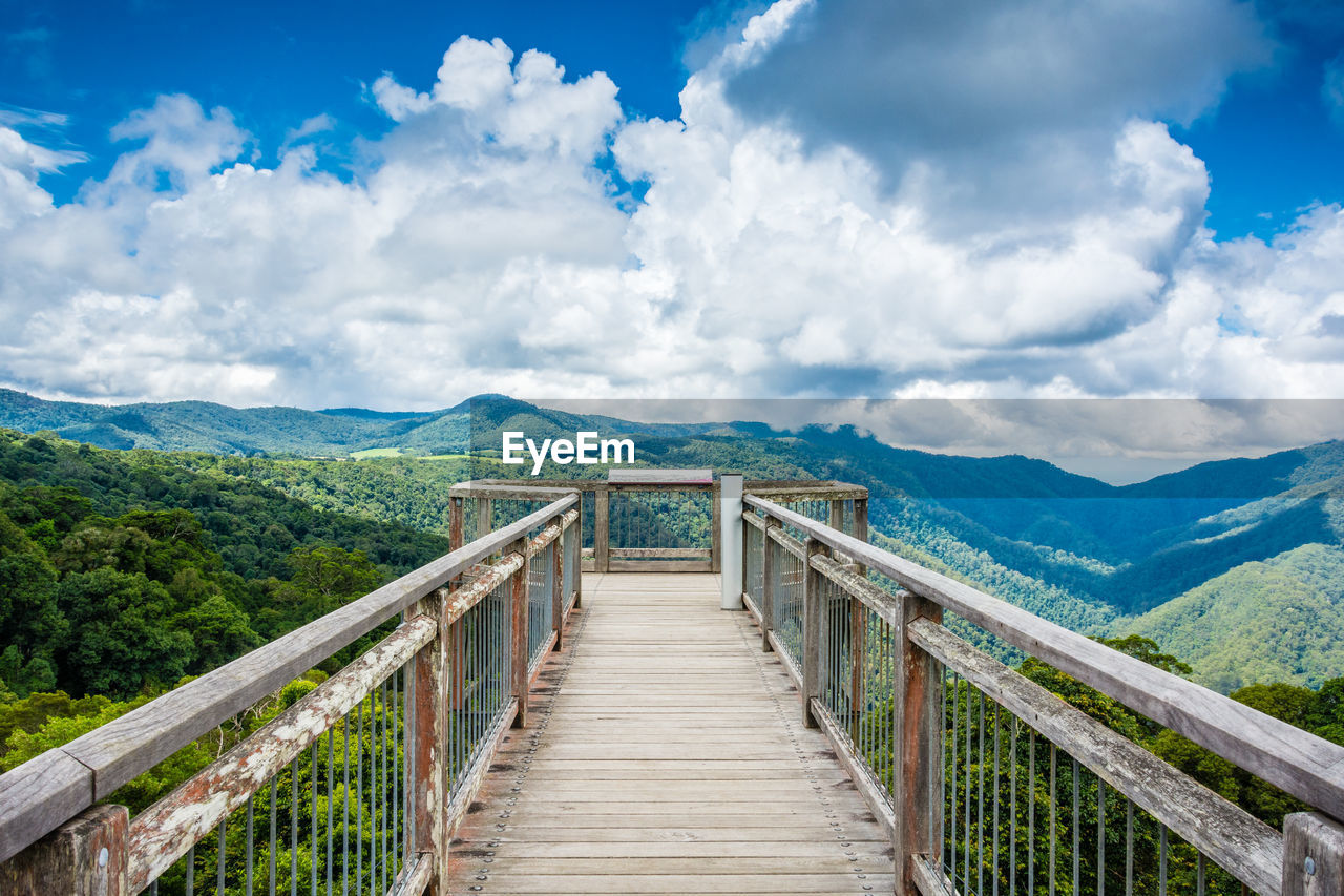 Boardwalk leading towards mountain against cloudy sky