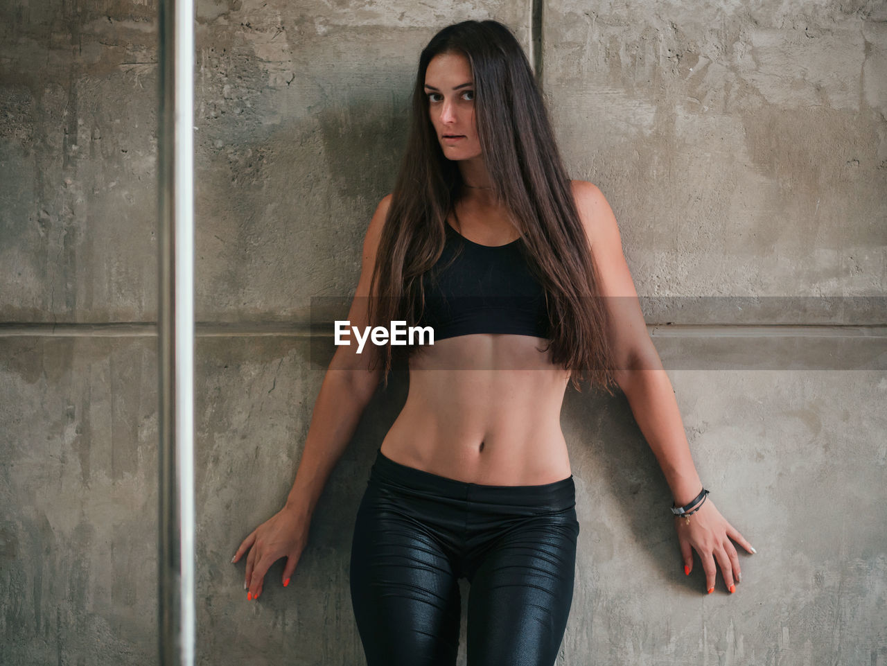 Portrait of sensuous pole dancer with long hair standing against wall in studio