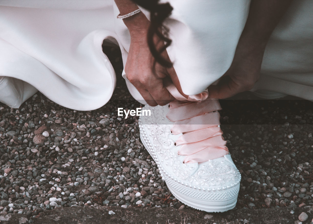 Low section of bride tying shoelace on field