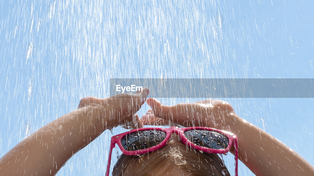 High section of girl in sunglasses under shower