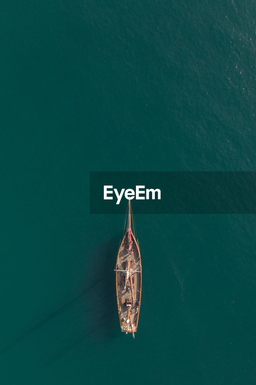  top down aerial view of a tall mast sailing boat on a calm turquoise ocean with copy space