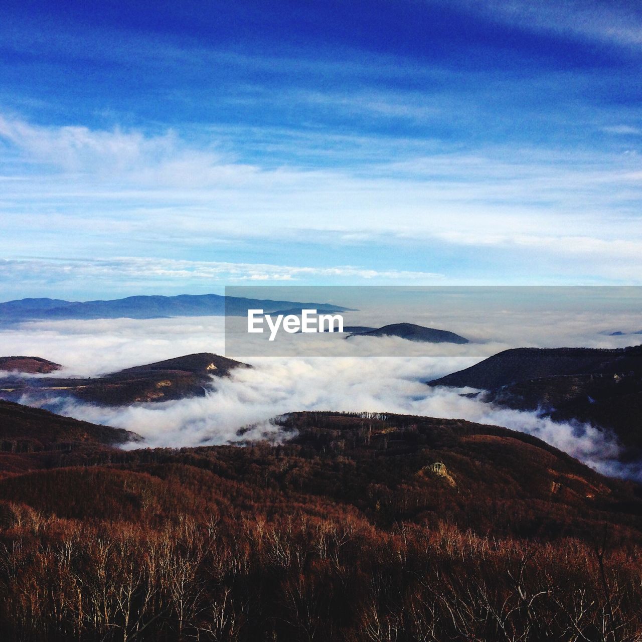 Scenic view of fog covered mountains against blue sky
