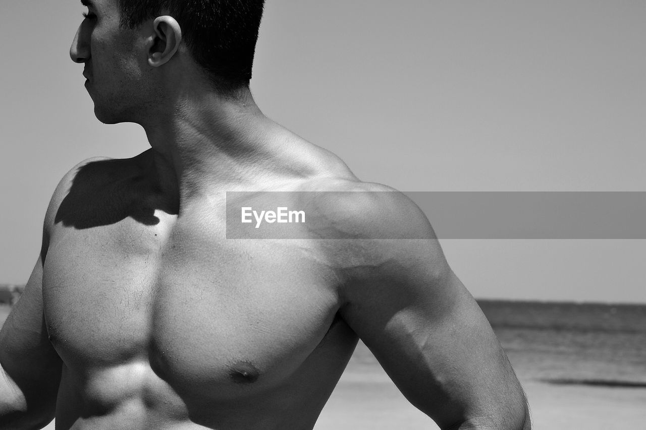 Shirtless man standing at beach against sky