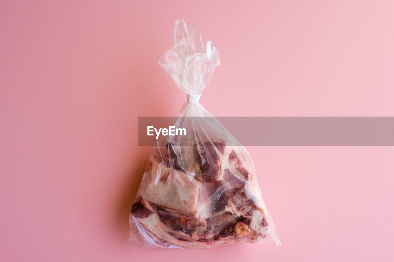Directly above view of fresh meat in plastic packet on pink background