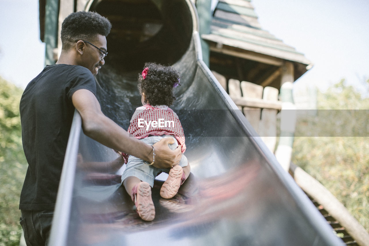 Father supporting daughter crawling up on slide at playground