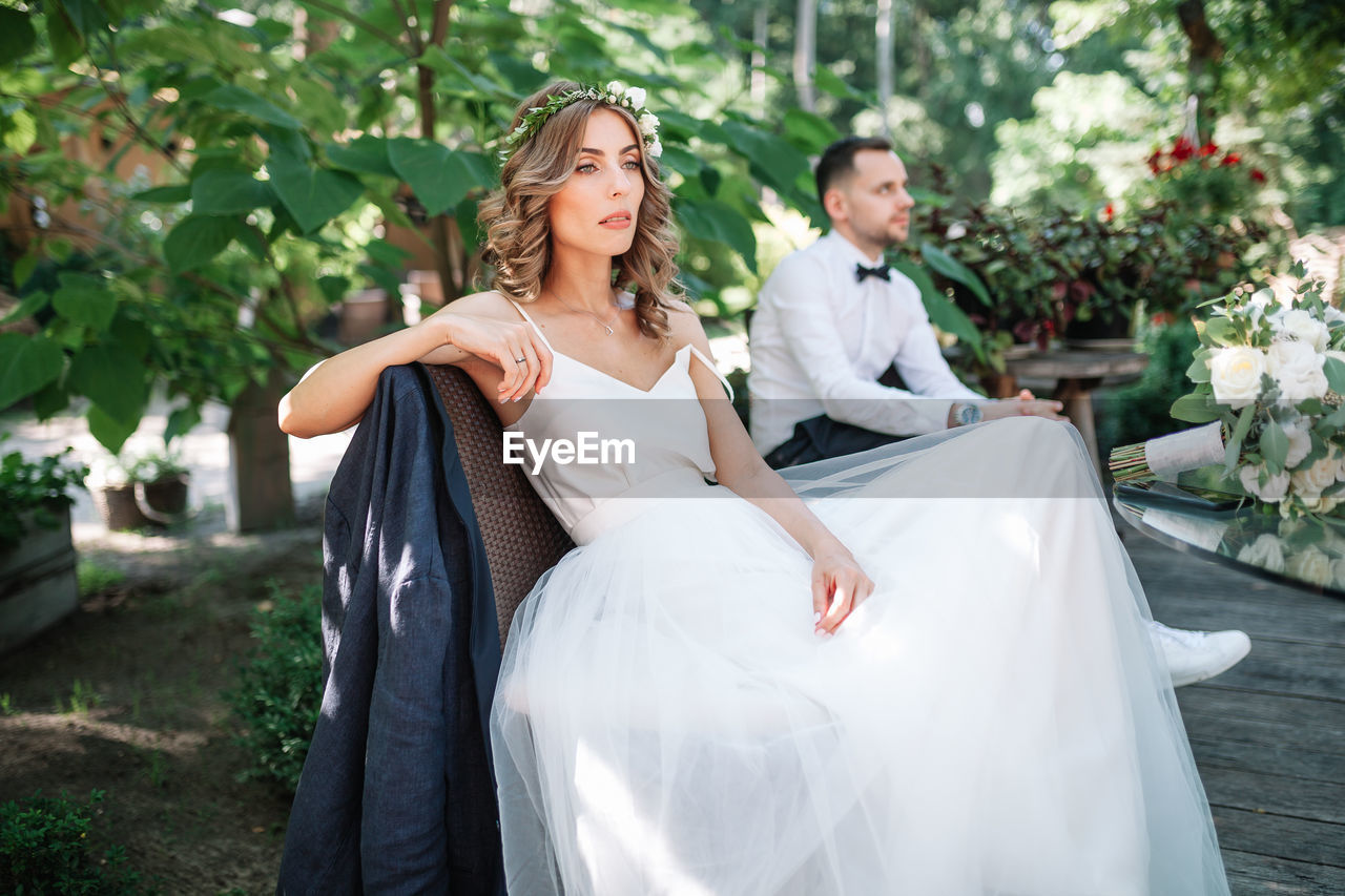 Thoughtful bride and bridegroom sitting on bench at park