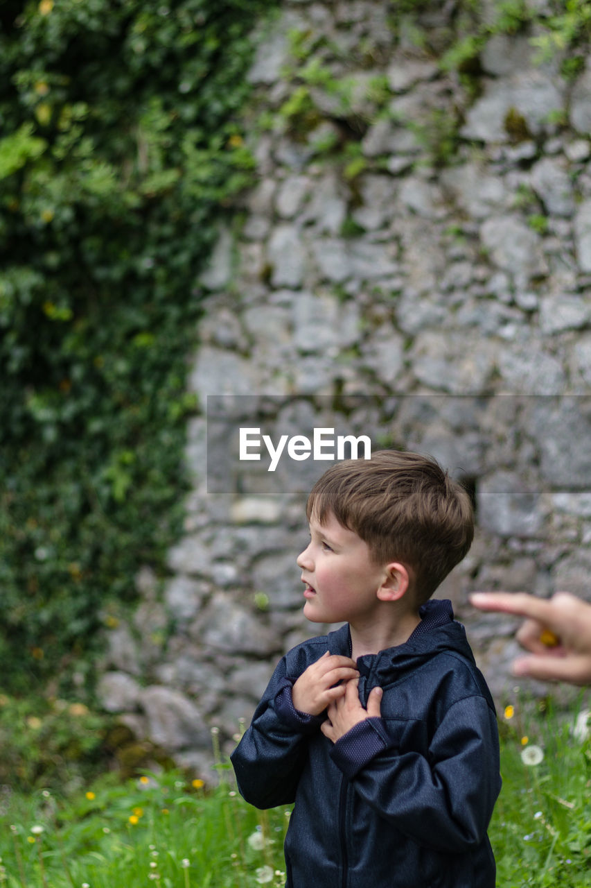 Boy looking away against stone wall