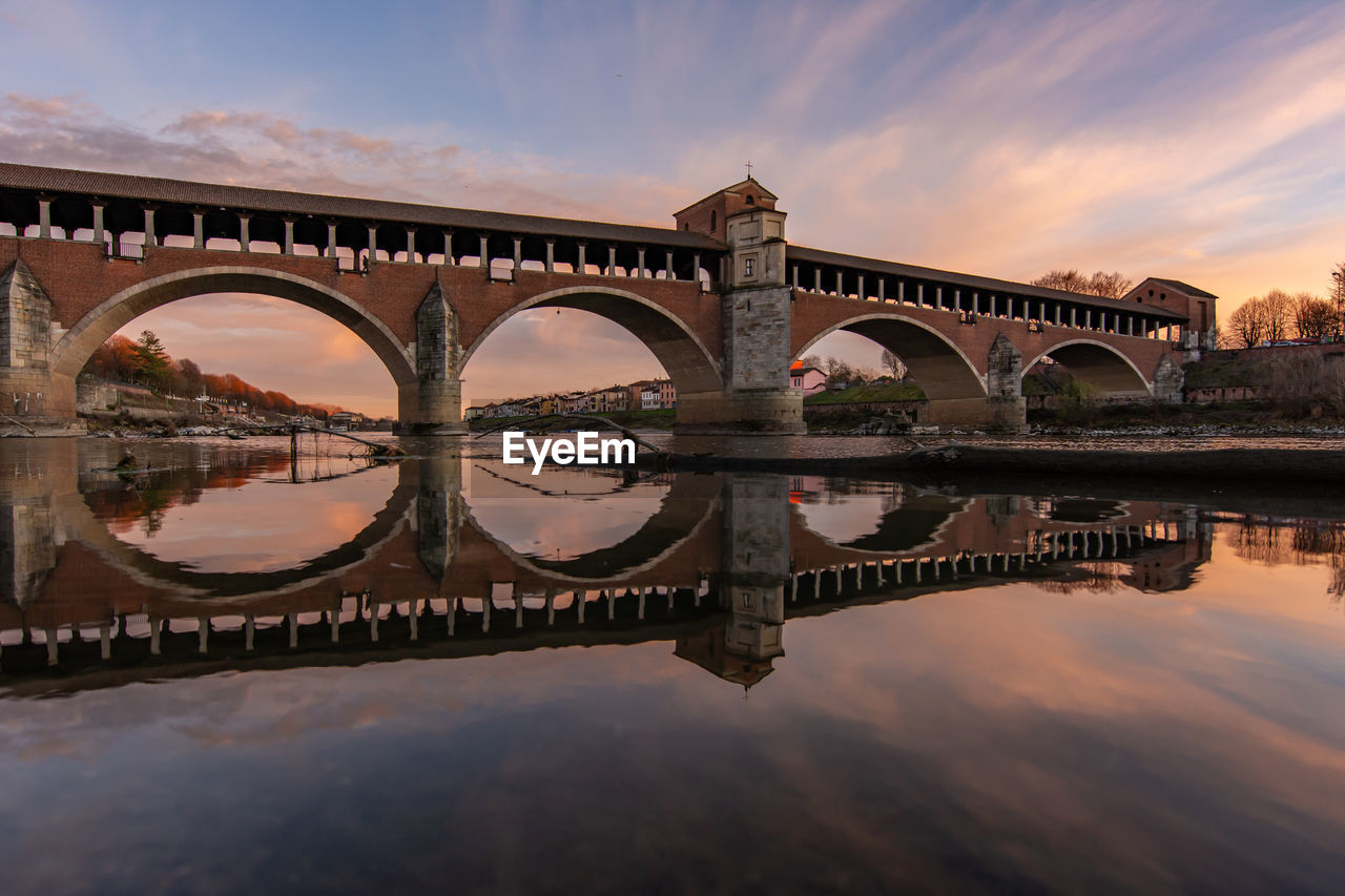 Arch bridge over river against sky during sunset