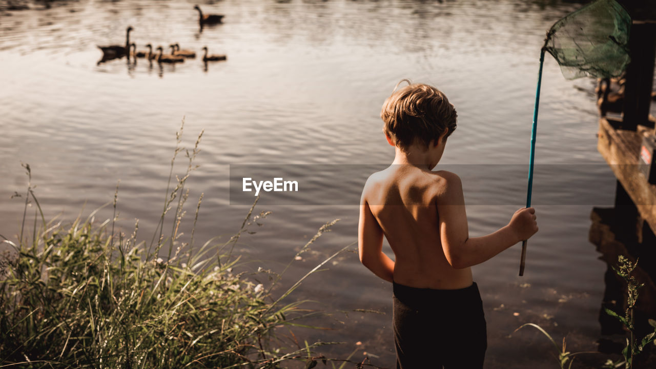 Rear view of shirtless boy standing in lake