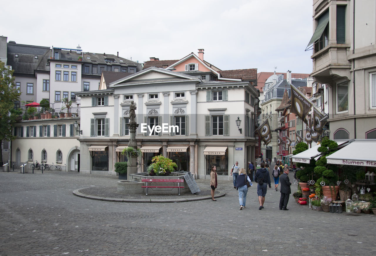 PEOPLE WALKING ON STREET AMIDST BUILDINGS IN CITY