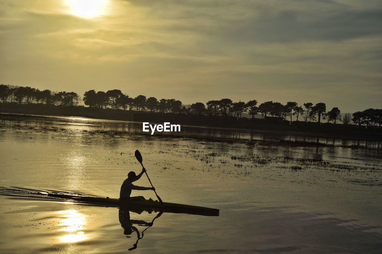 Man kayaking at lake against sky during sunset