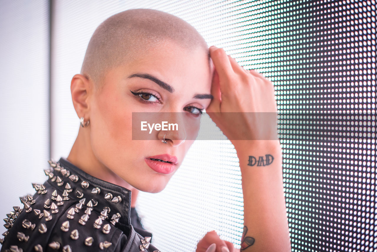 Portrait of young woman with shaved head standing against blue wall