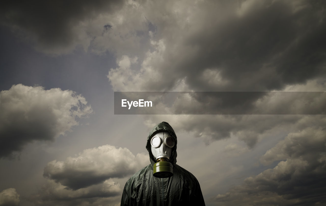 Portrait of person wearing gas mask while standing against cloudy sky