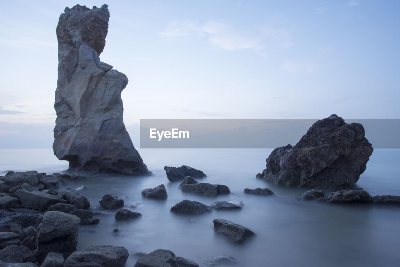 Low angle view of stack rocks in sea against sky at dusk