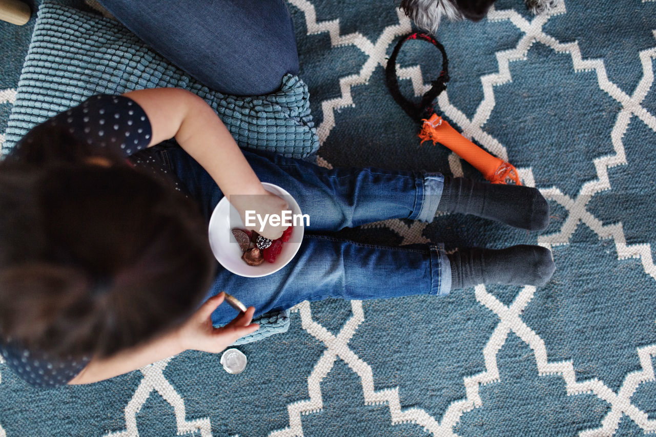 Directly above shot of girl eating candies while sitting on carpet at home