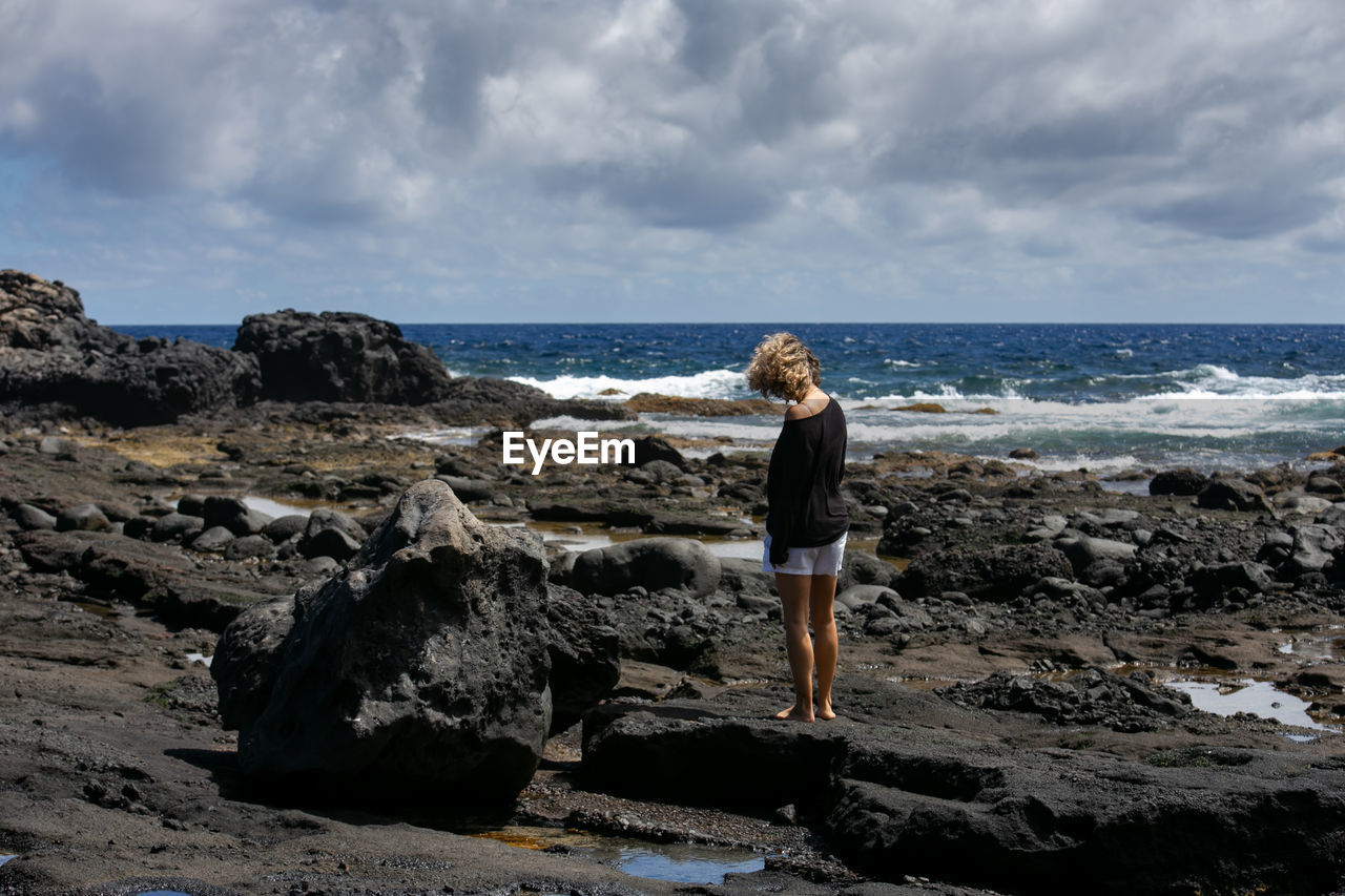 Full length of man standing on rock at beach against sky