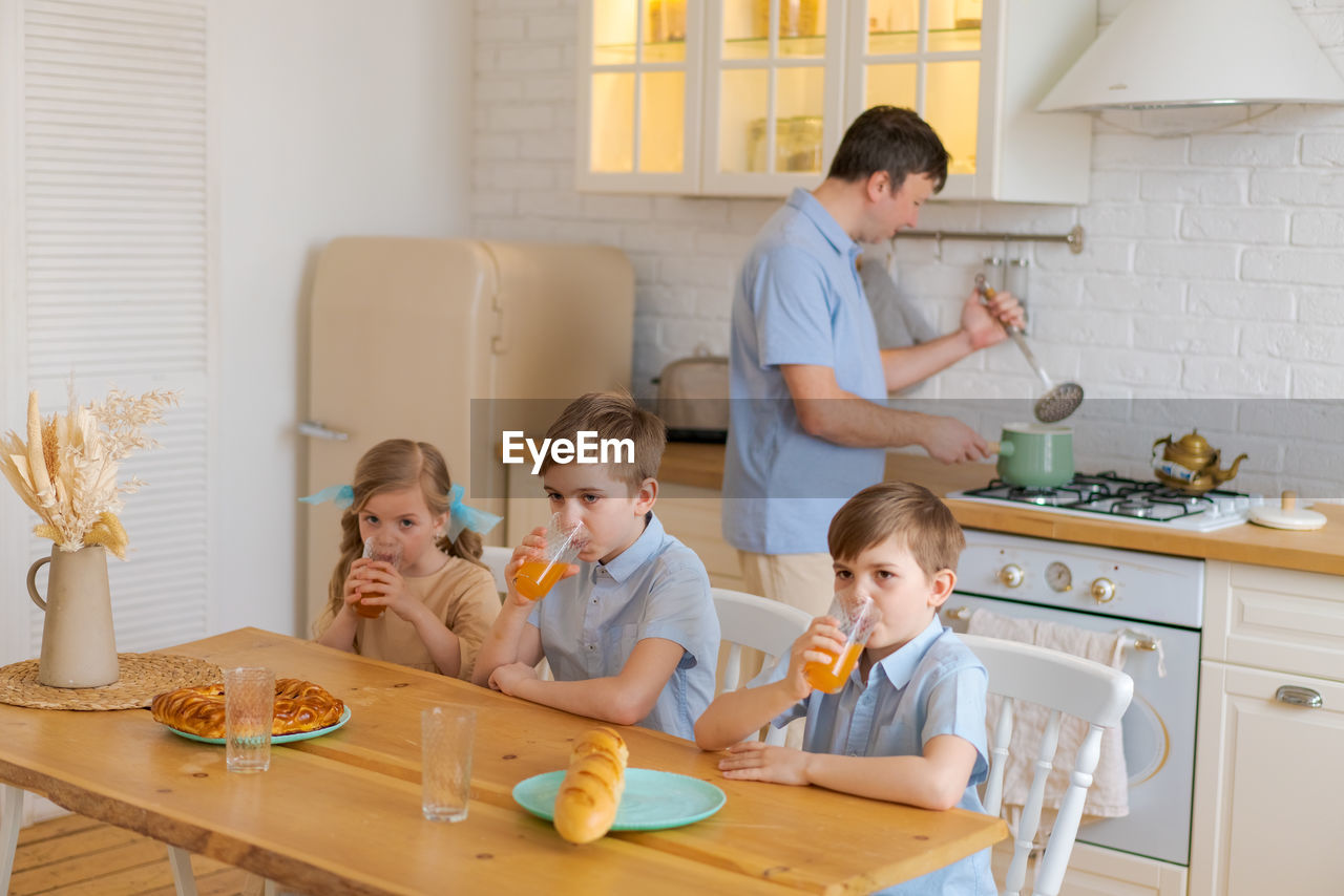 Caucasian mother sitting at table in kitchen children father serving preparing