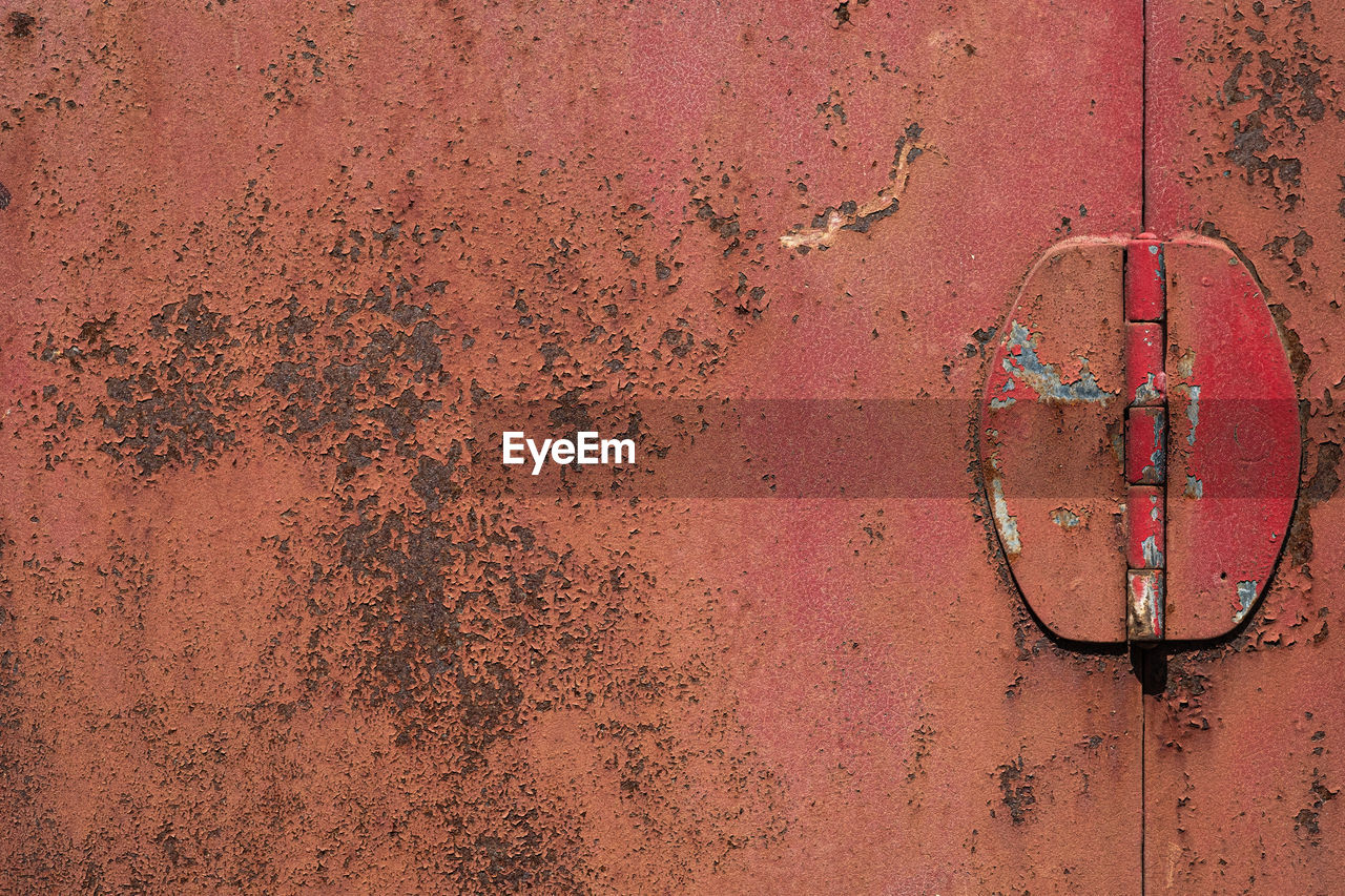 Old red iron door, rusted steel surface texture, rough peeling paint with door hinge