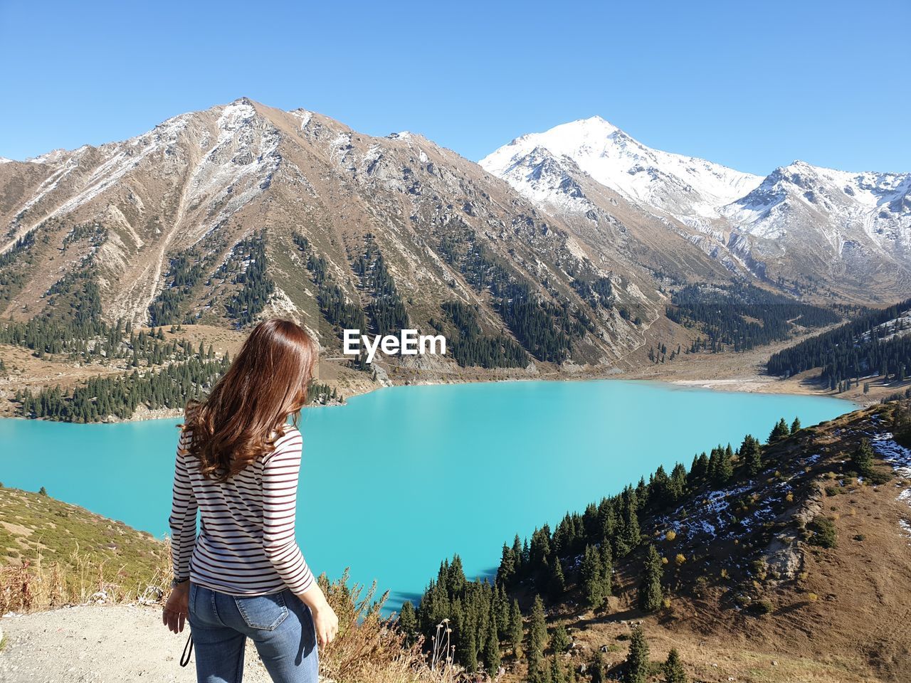 Woman standing on mountain by lake against sky